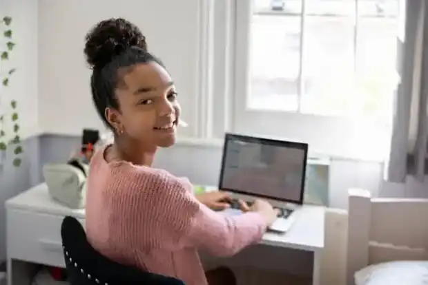 A learner smiling at her desk while working on a laptop at home