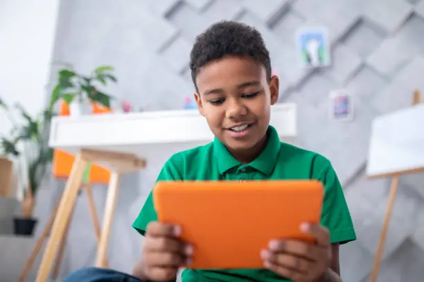 A primary school learner smiling while using the Saving Grace AI tutor on a tablet at his desk at home
